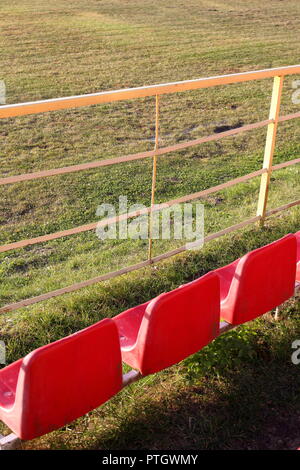 Trois sièges rouge vide, face à un terrain de football au début de l'automne Banque D'Images