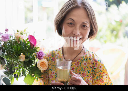 Portrait souriant, confiant senior woman boire le thé à côté de fleurs'' Banque D'Images