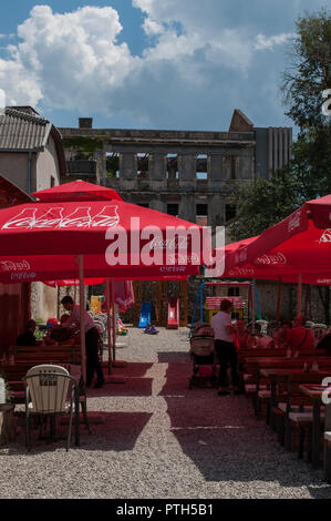 Mostar, Bosnie : une cour avec les tables d'un bar et d'un palais bombardé pendant la guerre de Bosnie (1992-1995) dans l'arrière-plan Banque D'Images