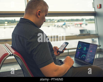 Portrait à l'aéroport avec ordinateur portable et smartphone dans la main d'analyser certaines données finances graphiques. travail mobile pour l'extérieur de la vie numérique Banque D'Images
