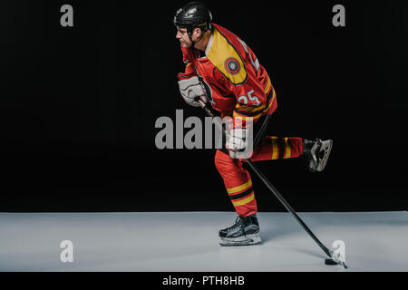 Vue latérale du jeune sportif jouer au hockey sur glace sur noir Banque D'Images