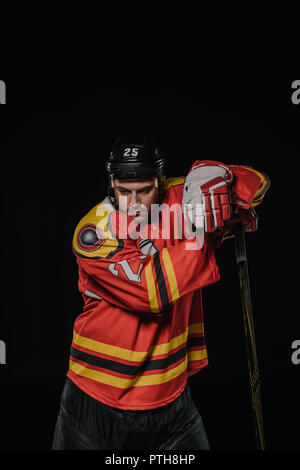 Joueur de hockey professionnel se penchant au stock de hockey et regardant en bas isolated on black Banque D'Images
