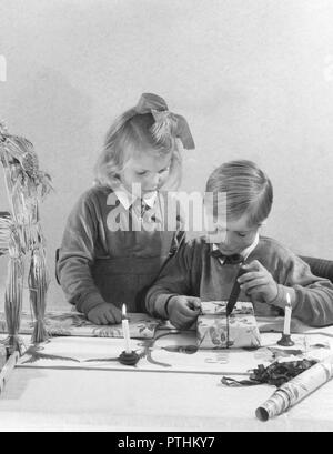 Noël dans les années 40. Deux enfants sont bien habillées envelopper des cadeaux de Noël. Le garçon est en train de fondre et de gouttes de cire sur le paquet cadeau. Un tampon est généralement mis dans la cire chaude avec les mots Joyeux Noël. Suède 1940 Banque D'Images