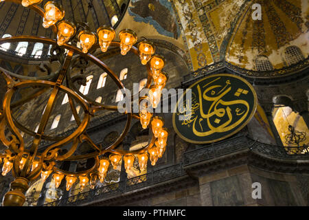 Vue sur le de l'chandaliers qui illuminent la nef principale de l'intérieur de l'Hagia Sophia Museum avec dome et cocarde calligraphiques en arrière-plan, Istanb Banque D'Images