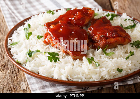 Vitrage poêlée de cuisses de poulet avec la sauce et le riz sur une assiette sur la table horizontale. Banque D'Images