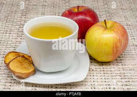 Vue rapprochée d'une tasse de thé d'apple avec deux pommes et déshydraté tranches du fruit avec une nappe à motifs à l'arrière-plan Banque D'Images