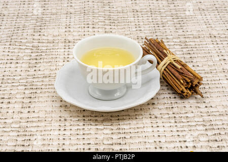 Vue rapprochée d'une petite tasse de thé avec une nappe à motifs en arrière-plan et un tas de petit bois à côté Banque D'Images