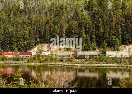 Les wagons de conteneurs sur un train de marchandises lourd passé en courant un lac au Canada avec des reflets dans l'eau. Banque D'Images