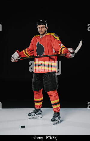 Sur toute la longueur du joueur de hockey sur glace professionnel holding bâton de hockey et looking at camera sur noir Banque D'Images