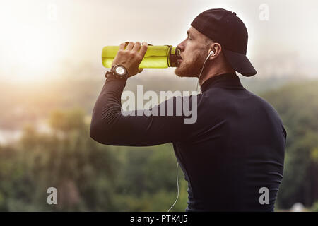 Gros plan homme sportif barbu se reposer et boire de l'eau après une séance d'entraînement. Banque D'Images