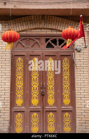Lanterne chinoise et d'un drapeau plus cadenassé la porte en bois avec du verre brisé dans la vieille ville de nouveau voisinage Uigher à Kashgar, ou Kashi, Xinjiang, Chine. Banque D'Images
