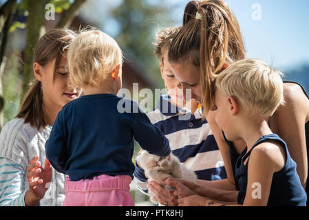 Jeune mère de quatre enfants à l'extérieur par une journée ensoleillée de câliner leur animal à fourrure lapin. Banque D'Images