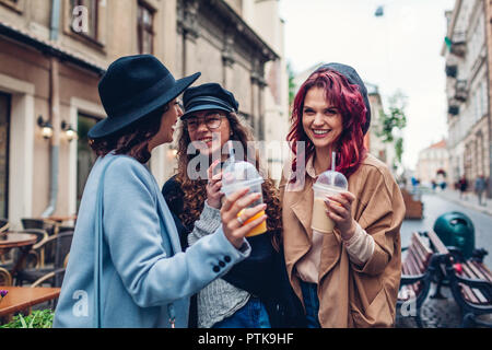 Trois amies ayant des boissons à l'extérieur. Les femmes clinking café, jus d'orange et tasses à thé Banque D'Images