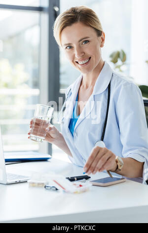 Smiling female doctor holding verre d'eau et en tenant comp at table in office Banque D'Images