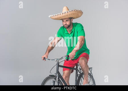 Bel homme au sombrero mexicain riding bike sur gris Banque D'Images