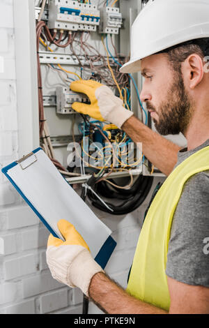 Beau electrician holding clipboard et contrôler le panneau électrique dans le couloir Banque D'Images