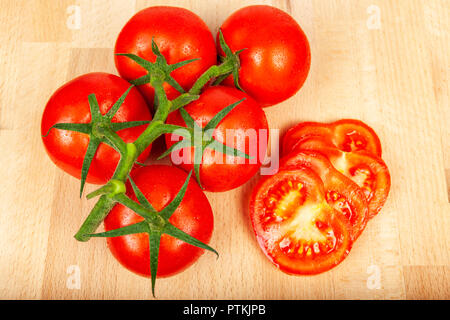 Tomates mûres fraîches sur une vigne sur un bloc de bois planche de côté quelques tranches jucy haché Banque D'Images