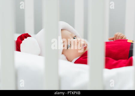 Gros plan sur la belle petite baby in santa suit lying in crib Banque D'Images