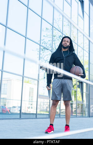 Low angle view of african american sportsman holding basketball ball on street Banque D'Images