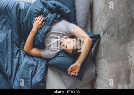 Portrait de jeune homme séduisant dormir sous une couverture dans son lit à la maison Banque D'Images