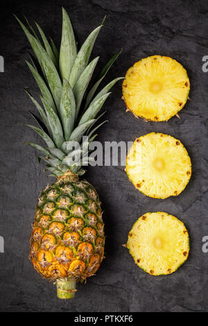Ananas frais mûrs et les sections coupées sur fond sombre, la composition verticale, vue du dessus Banque D'Images