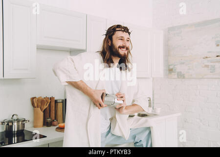 Jésus souriant avec des grains de café de meulage dans coffeemill mains manuel dans la cuisine à la maison Banque D'Images