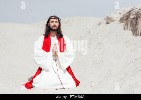 Les yeux fermés, Jésus debout sur les genoux sur le sable et en priant dans le désert Banque D'Images