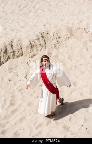 Portrait de Jésus en robe, ceinture rouge et couronne d'épines sur le sable du désert en marche Banque D'Images