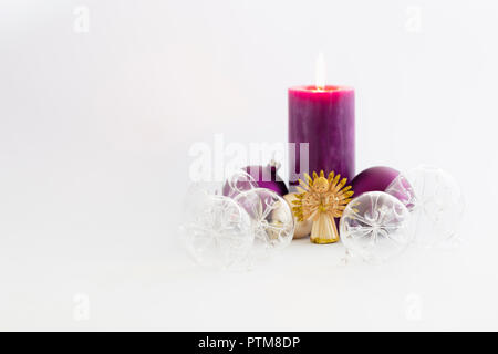 La vie toujours avec de belles boules de noël en verre transparent décoratif, une couleur violette bougie brûlante et une paille ange sur fond blanc Banque D'Images