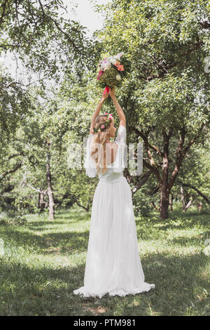 Vue arrière de la belle jeune femme en robe de mariage bouquet jetant dans park Banque D'Images