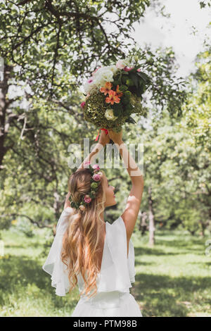 Vue arrière de la belle jeune femme jetant mariage bouquet in park Banque D'Images