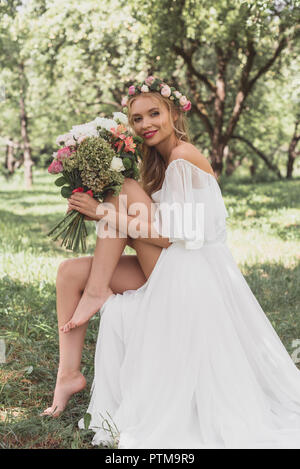 Belle jeune barefoot bride holding bouquet of flowers and smiling at camera Banque D'Images