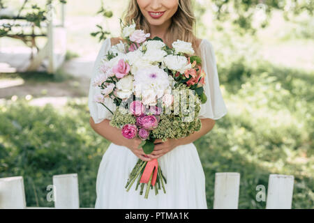 Cropped shot of happy blonde bride holding bouquet de mariage magnifique en plein air Banque D'Images