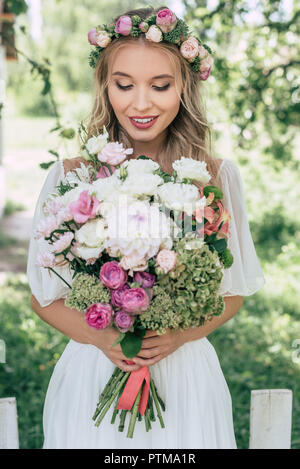 Belle couronne de fleurs en mariée smiling holding beau bouquet de fleurs à l'extérieur Banque D'Images