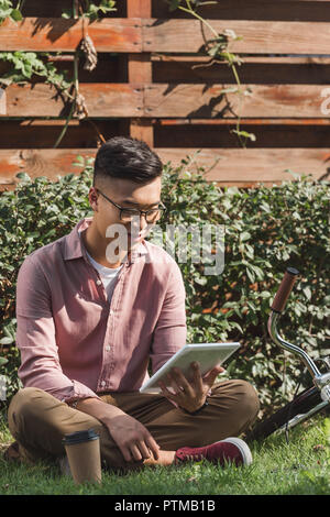 Asian man in eyeglasses sitting on Green grass in park Banque D'Images