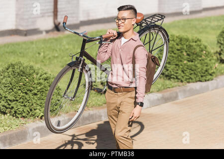 Smiling young man carrying bicycle en marchant sur la rue Banque D'Images