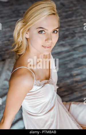 High angle view of beautiful blonde girl sitting and smiling at camera dans la chambre Banque D'Images