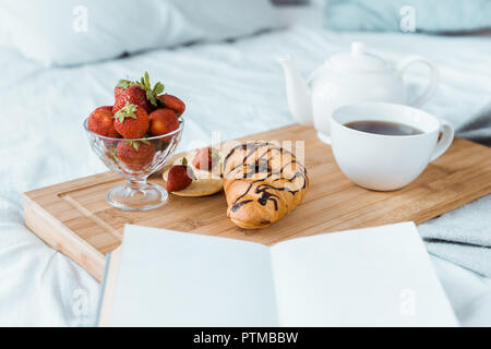 Petit-déjeuner appétissant de fraises, croissant et café sur plateau en bois on bed Banque D'Images