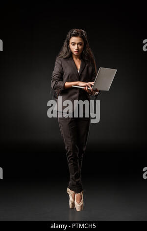 Businesswoman in suit et chaussures de ballet avec ordinateur portable sur fond noir Banque D'Images