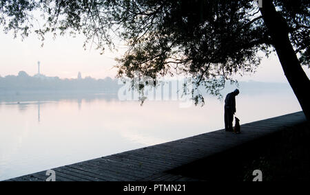 Hanovre, Basse-Saxe. 10 Oct, 2018. Un homme s'attarde à le Maschsee, sur lesquelles la brume se dissipe tôt le matin avant le lever du soleil. Credit : Julian Stratenschulte/dpa/Alamy Live News Banque D'Images