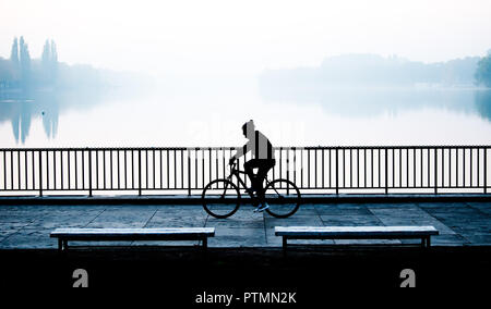 Hanovre, Basse-Saxe. 10 Oct, 2018. Randonnées cyclistes le long de la rive nord du lac Maschsee, sur lesquelles la brume se dissipe tôt le matin avant le lever du soleil. Credit : Julian Stratenschulte/dpa/Alamy Live News Banque D'Images