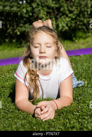 Petite fille en colère se trouve sur l'herbe verte et de penser à Banque D'Images