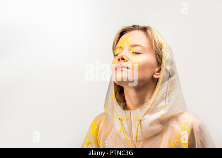 Belle femme en imperméable peint avec peinture jaune aux yeux clos permanent isolated on white Banque D'Images