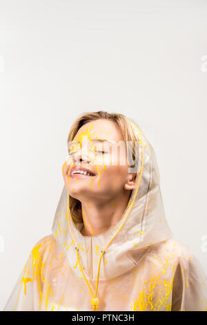 Happy woman in raincoat peint avec peinture jaune aux yeux clos permanent isolated on white Banque D'Images