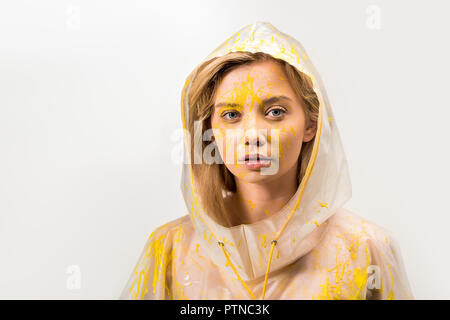 Belle femme en imperméable peint avec peinture jaune looking at camera isolated on white Banque D'Images