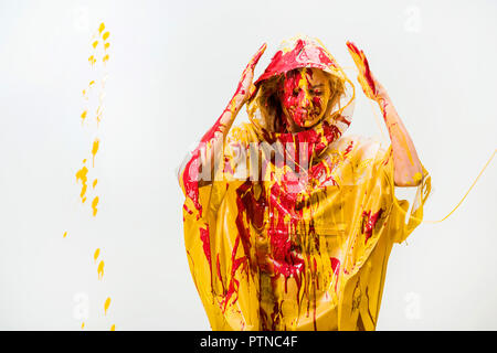 Belle femme en imperméable peint avec les peintures jaune et rouge la protection de tête avec mains isolated on white Banque D'Images