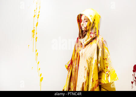 Belle femme en imperméable peint avec les peintures jaune et rouge debout dans hood isolated on white Banque D'Images