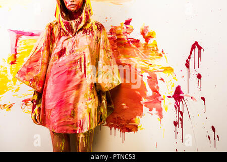 Portrait of woman standing in raincoat peint avec les peintures jaune et rouge près de wall Banque D'Images