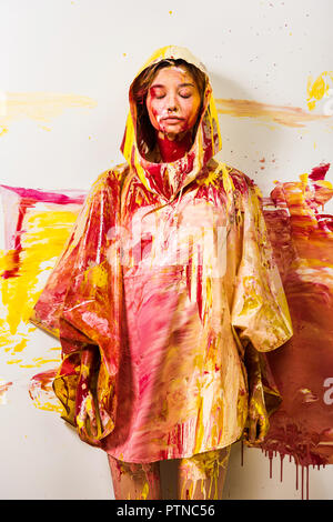 Belle femme en imperméable peint avec les peintures jaune et rouge debout avec les yeux fermés Banque D'Images