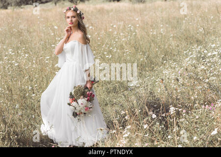 Belle pensive young bride en robe de mariage et la couronne de fleurs bouquet de fleurs tout en se tenant à l'extérieur Banque D'Images